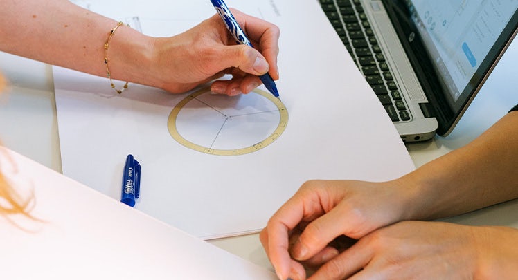 A woman is drawing a circle on a piece of paper.